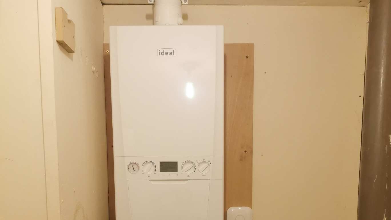 Ideal combi boiler on a timber backing board inside a cupboard, with the flue running up from the top